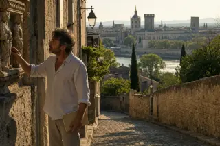 Local artisan examining a medieval stone relief in a narrow Villeneuve-lès-Avignon street, golden light and distant Avignon skyline in background.