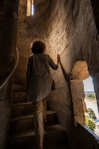A person gently touches a carved stone wall in a narrow passage near an old fortress, with warm golden light and a peaceful atmosphere.